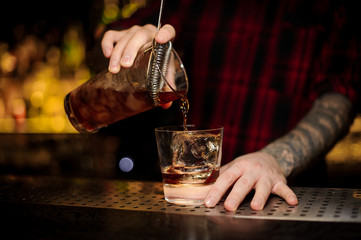 Fototapeta na wymiar Bartender pouring fresh strong whiskey cocktail into a glass
