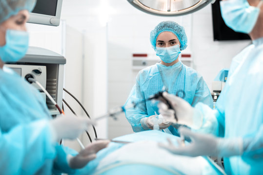 Waist up portrait of young lady in protective mask and sterile gloves providing respiratory support to sick person during surgical operation