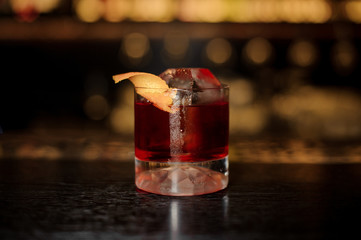 Elegant glass of tasty fresh and strong whiskey cocktail decorated with orange peel on bar counter