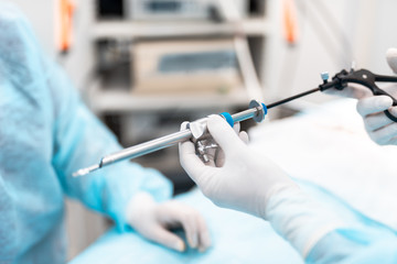 Close up of doctor hands in sterile gloves attaching laparoscopic trocar to surgical grasper