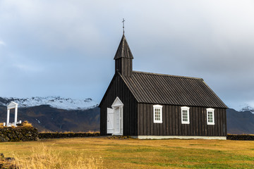 Fototapeta na wymiar Small Black Wooden Church with Cloudy Mountains in Background in West Iceland on a Rainy Fall Day