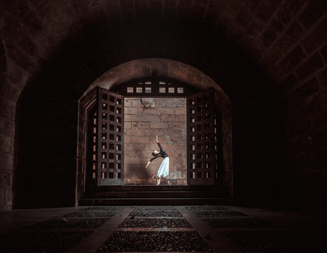 Young ballerina training between big wood doors near brick wall
