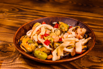 Ceramic plate with different sea food and olives on wooden table