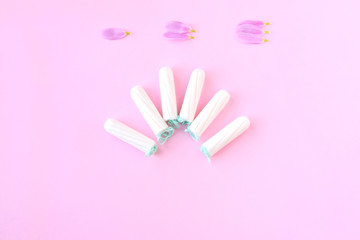 Tampons with selective focus on blurred pink background with pink flower petals. Woman hygiene for period days, menstrual mothly cycle. Protective care for woman health.