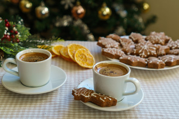 Two espresso in white cups on a table next to gingerbread cookies on a cozy background decorated for Winter Holidays. Having coffee on Christmas day.