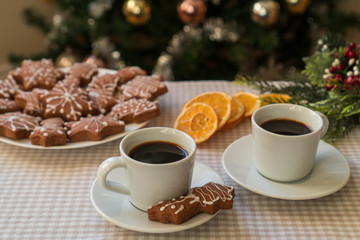 Two cups of hot coffee on a table next to gingerbread cookies on a cozy background decorated for Winter Holidays. Having coffee on Christmas day.