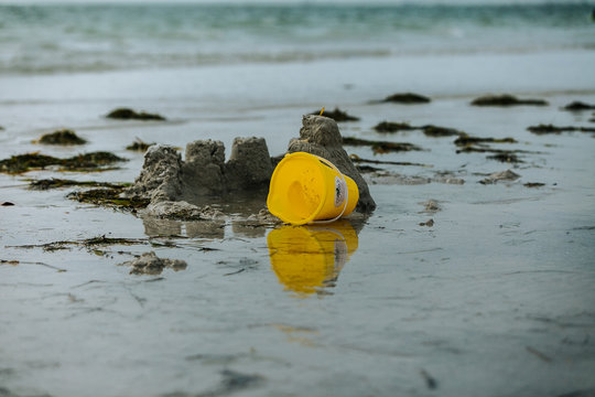Yellow bucket reflecting on the beach next to a sand castle