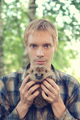 portrait of a young man holding a prickly hedgehog © tntk