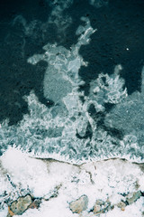Ice fragments under thin layer of frozen river water. Dark blue natural background