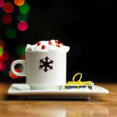 Christmas coffee with whipped cream and a small gift on the background bokeh lights