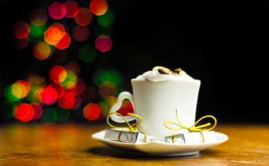 Christmas coffee with whipped cream and a small gift on the background bokeh lights