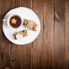 Homemade granola oatmeal energy bars, and cup of tea wyth orange star on white plate, healthy snack, copy space on wood desk