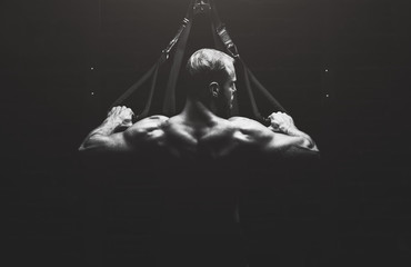 A muscular man holds a strap in her hand for the suspension training in the gym. TRX exercises. Sports concept and healthy lifestyle.