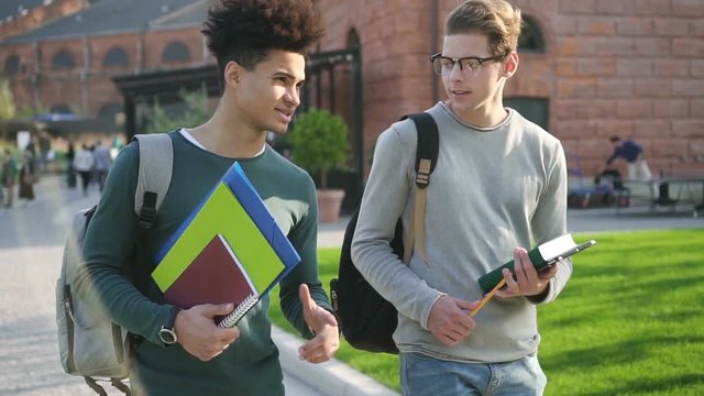 Two best male friends are walking and talking near campus. Students from one faculty and group are chating about girls, new video games, sport and laugh together after intense studying at the