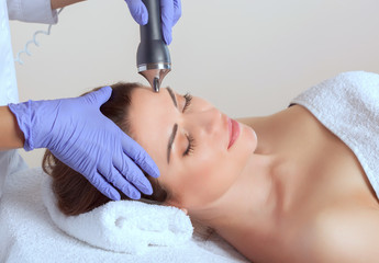 The cosmetologist makes the procedure an ultrasonic cleaning of the facial skin of a beautiful,...