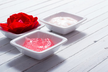 skin care creams and rose on white wooden table