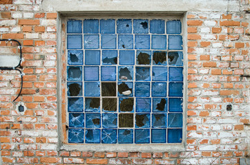 broken window with the remains of blue glass blocks in the old brick wall