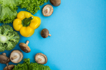 Mushrooms shiitake and vegetables on the yellow cutting board on the blue background.Top view.Copy space.Healthy food ingredients.