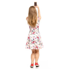 Fototapeta premium Beautiful woman in dress with flowers print and sneakers showing of positive emotions with smartphone mobile phone selfie back view on white background isolation