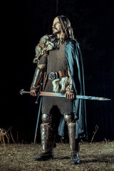 Long haired knight with the two-handed sword. Rocks on the background.