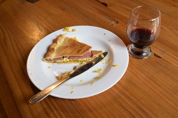 on the table there is an unfinished red wine in a glass and a piece of cake