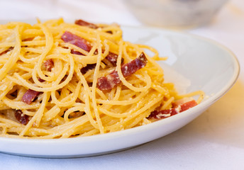 Pasta carbonara spaghetti with ham, bacon and fresh parmesan on the white plate in restaurant in Catania, Sicily, Italy
