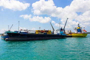 Fototapeta premium Loading and unloading of containers on commercial cargo ship in sea port on a bright sunny day. Background for import ,export cargo, nautical vessel transport and industry logistic. Safety first.