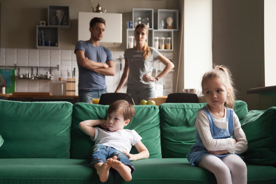 Upset offended sister, daughter sitting separately on couch with arms crossed with toddler brother on couch, sofa after fight about tv channel, cartoon choice, little girl and boy ignoring each other