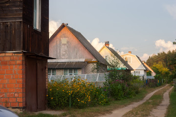 Rustic sandy unpaved street with manor houses along. Dense low-rise rural buildings.