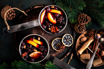 hot mulled wine cooked in two saucepan with spices, orange and cranberries on the table with...