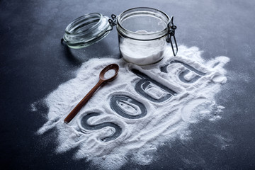 baking soda scattered from a glass jar on a dark background - obrazy, fototapety, plakaty