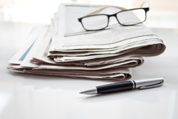 A stack of newspapers with glasses and pencil. Shallow depth of field.