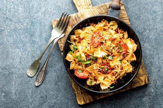 pasta farfalle with roasted meat and tomatoes in a frying pan