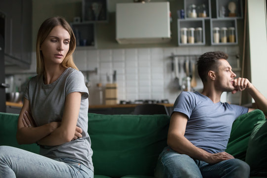 Offended upset man and woman sitting separately on couch, sofa in living room, wife looking with insult at husband, bad relationships, quarrel, break up