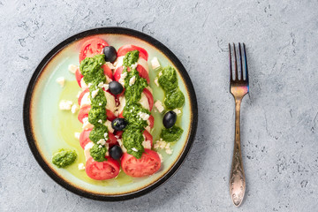 Tomato and mozzarella caprese salad and pesto sauce with olives on gray table