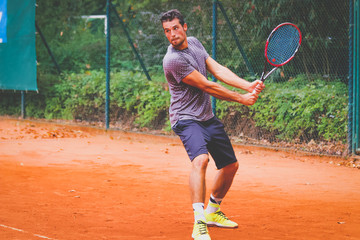 Junger Tennisspieler holt zu einem Rückhandschlag aus - gespielt auf einem Sandplatz Court