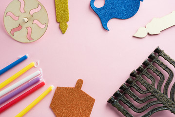 Image of jewish holiday Hanukkah with wooden dreidels (spinning top) , candles, menora, children's stickers glitter craft- jug of Chanukah and candles on pink background.