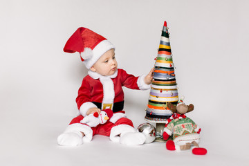 Little girl wearing santa claus red dress sitting on the floor holding small Christmas ball and smiles over white background,Christmas concept.
