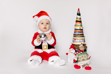 Little girl wearing santa claus red dress sitting on the floor holding small Christmas ball and smiles over white background,Christmas concept.