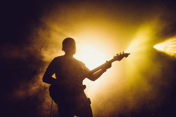 Guitarist silhouette on a stage in a smoke and backlights playing rock music