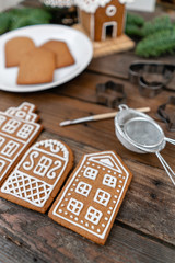 A lot of ginger biscuits in the form of European houses on brown wooden table. Decorated with white sweet glaze. Christmas mood, winter morning.