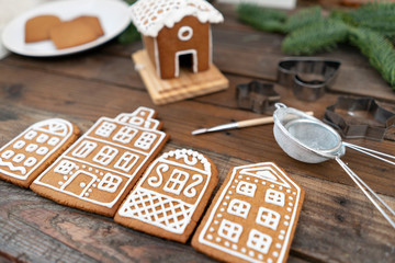 A lot of ginger biscuits in the form of European houses on brown wooden table. Decorated with white sweet glaze. Christmas mood, winter morning.