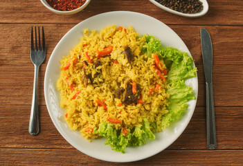 Uzbek pilaf with lamb, spices and seasonings, decorated with lettuce leaves on a wooden background