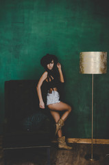  sensual woman in jeans shorts and hat standing near green chair and posing