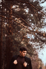 Young man with coat covering his shoulders in the autumn forest.