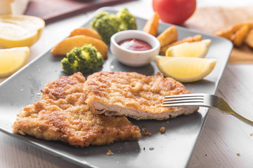Pork chop with country-style potatoes and fresh vegetables on a grey plate on a white table, top view
