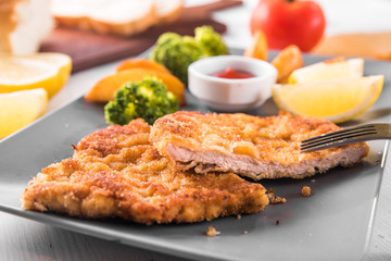 Pork chop with country-style potatoes and fresh vegetables on a grey plate on a white table