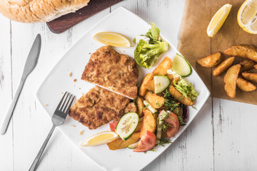 Pork chop with country-style potatoes and fresh vegetables on a white plate on a white table, top view