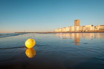 Bright yellow buoy on the beach of Oostende with city skyline in the background
