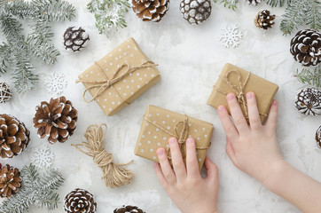 Top view. Flat lay children's hands hold gift boxes, cones, rope, fir branches and snowflakes on white background. Winter.